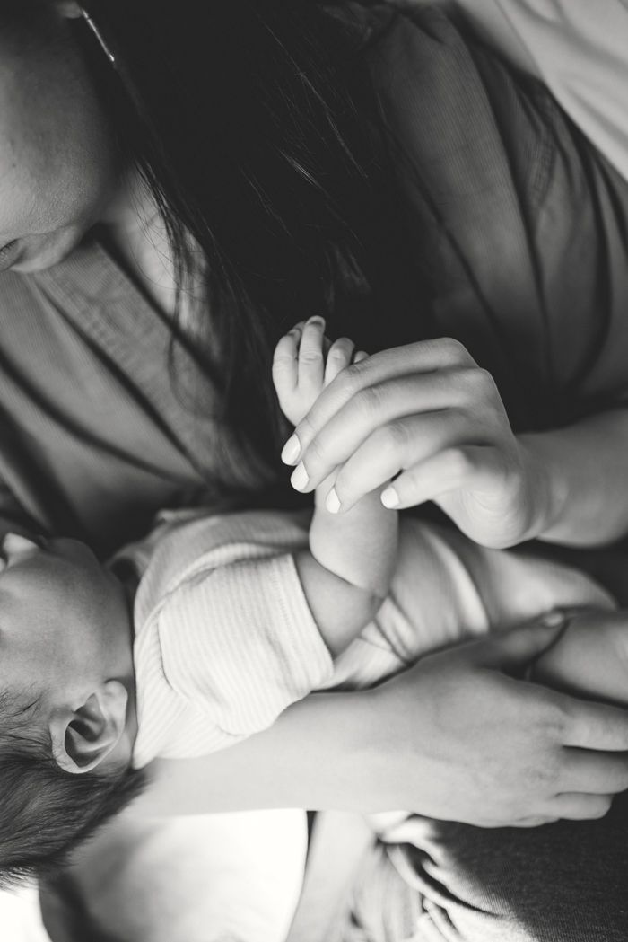 Black and white photo of a mother cradling her newborn baby, gently holding the infant's tiny hands.