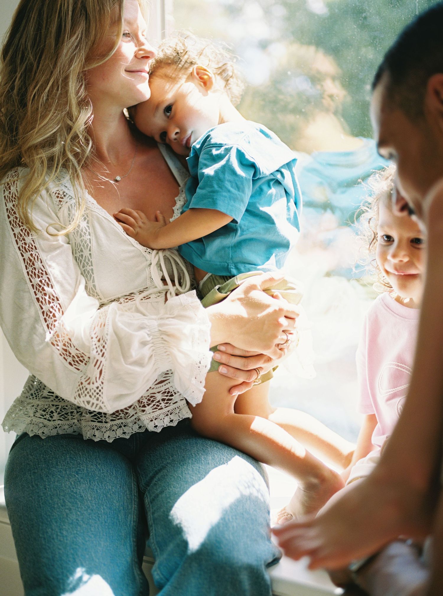 A tender moment captured in soft natural light as a mother in white lace and denim embraces her child.