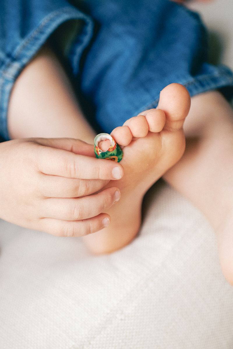 Close-up of a child's foot being held gently, with a small colorful ring placed on one tiny toe.