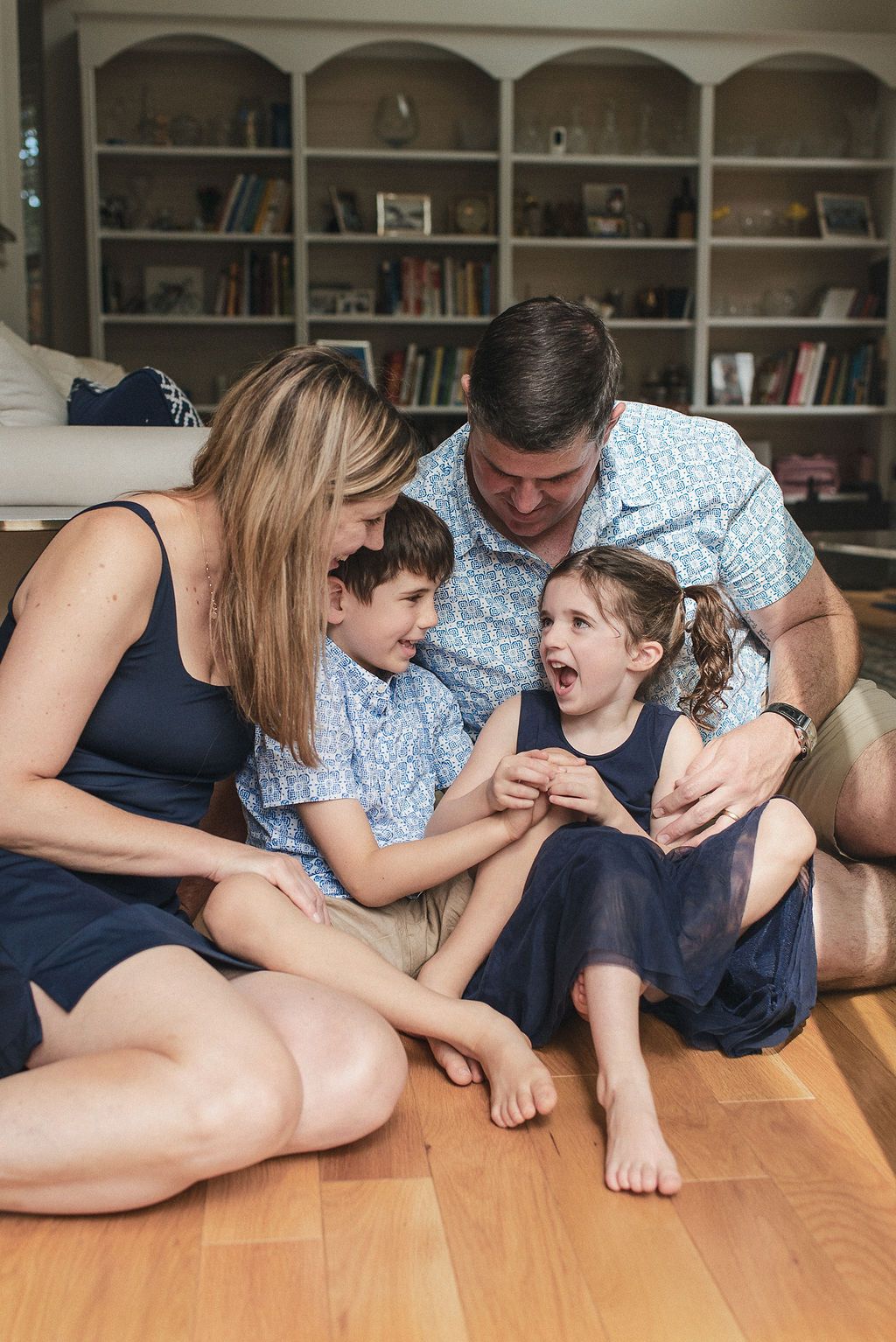 Family lying on hardwood floor together in casual playful moment at home.