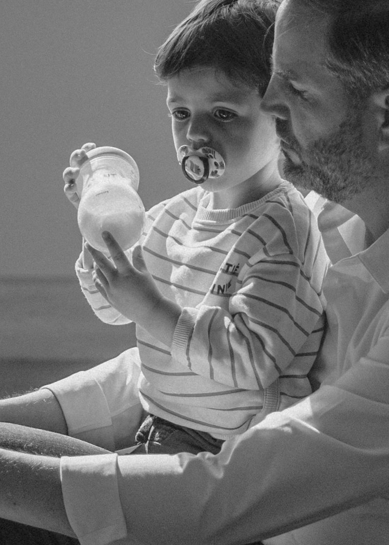 Child wearing a striped shirt leans forward while wearing a protective face mask during a medical consultation session.