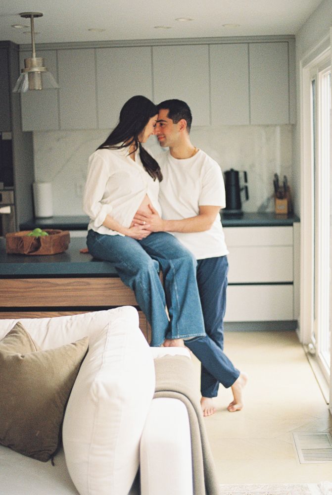 Couple in white shirts and jeans sitting together on a couch in a minimalist living room.