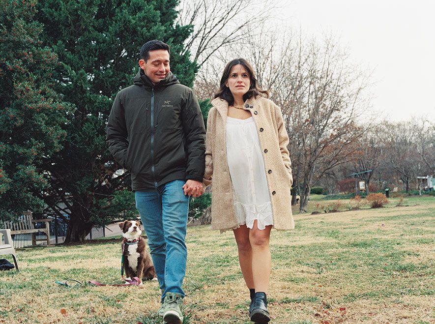 A couple and their dog walk together through a grassy field on an overcast autumn day.