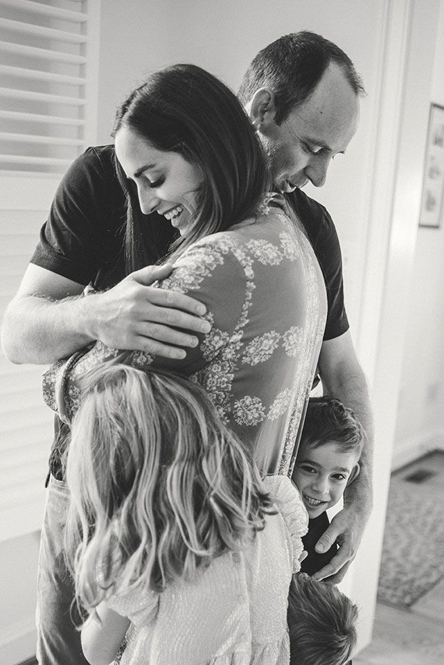 A black and white candid photo of a family sharing an intimate embrace and laughing together.