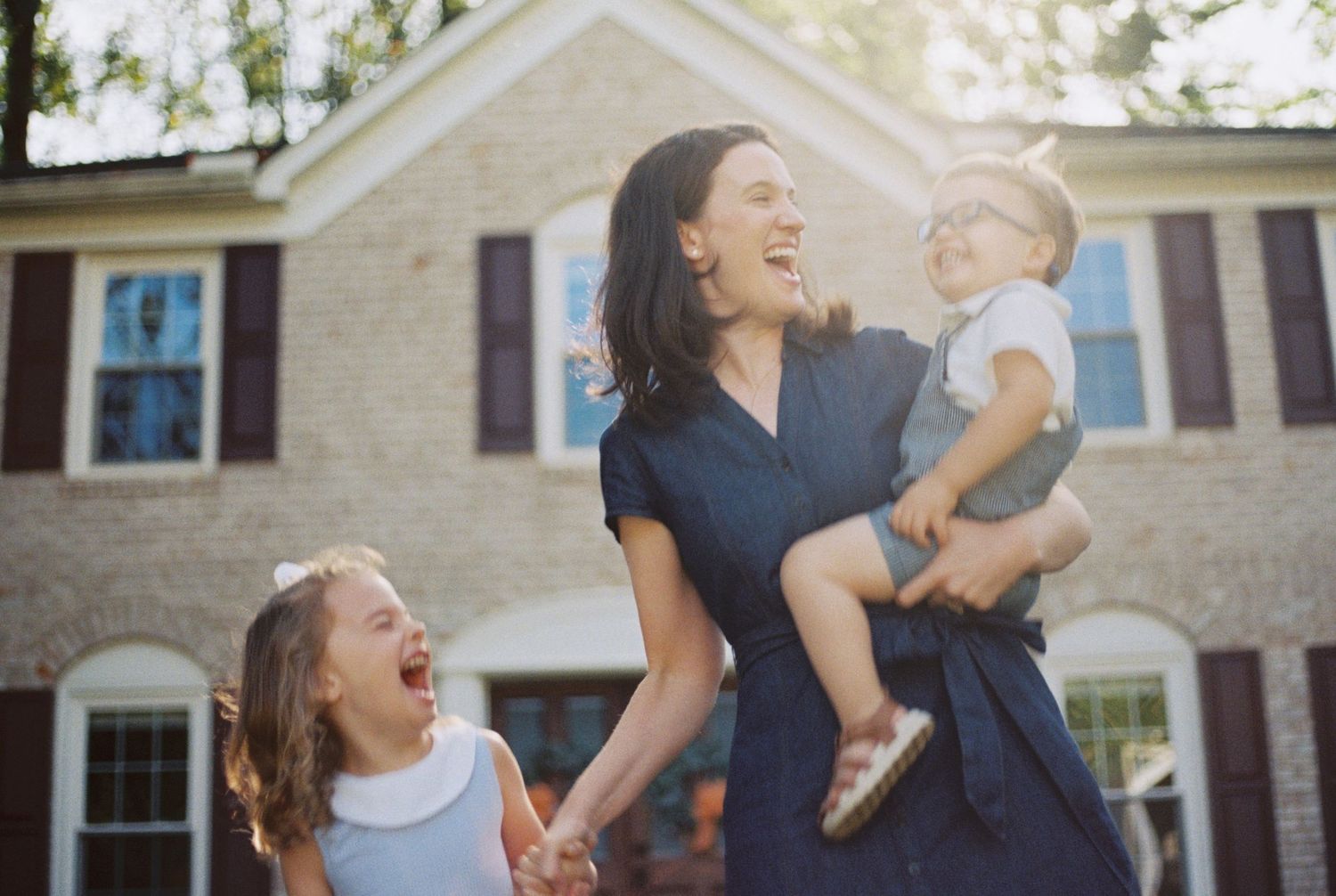 A joyful family plays together outdoors in front of a white house on a sunny day.