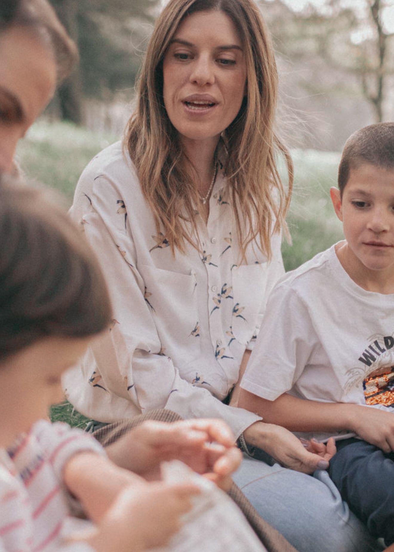 A family sits together on a blanket outdoors for a picnic while sharing food and enjoying nature.
