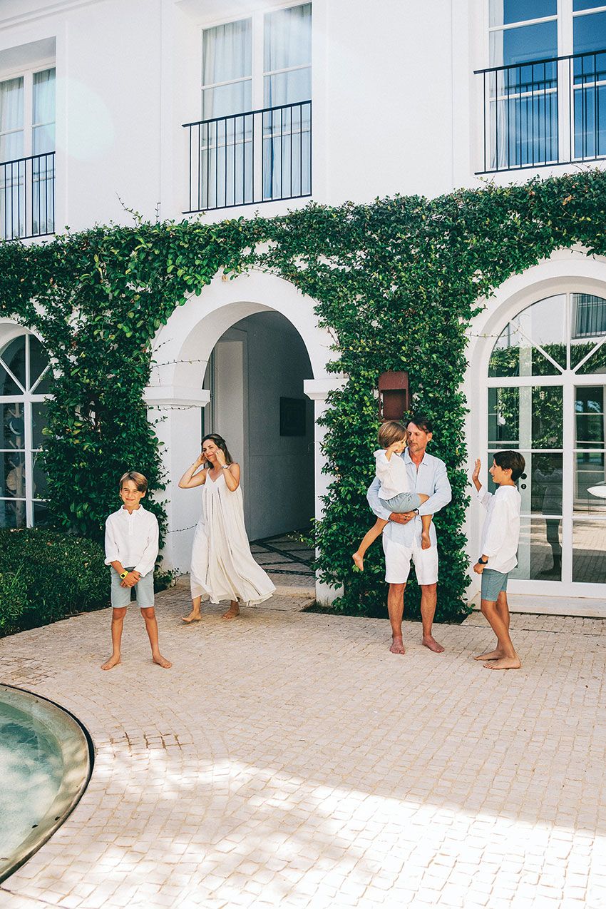 People dancing and enjoying themselves on a white stone patio surrounded by lush green hedges and arched architecture.