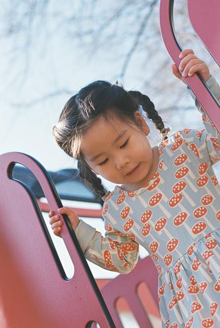 Young Asian girl with braided pigtails climbing pink playground equipment outdoors.
