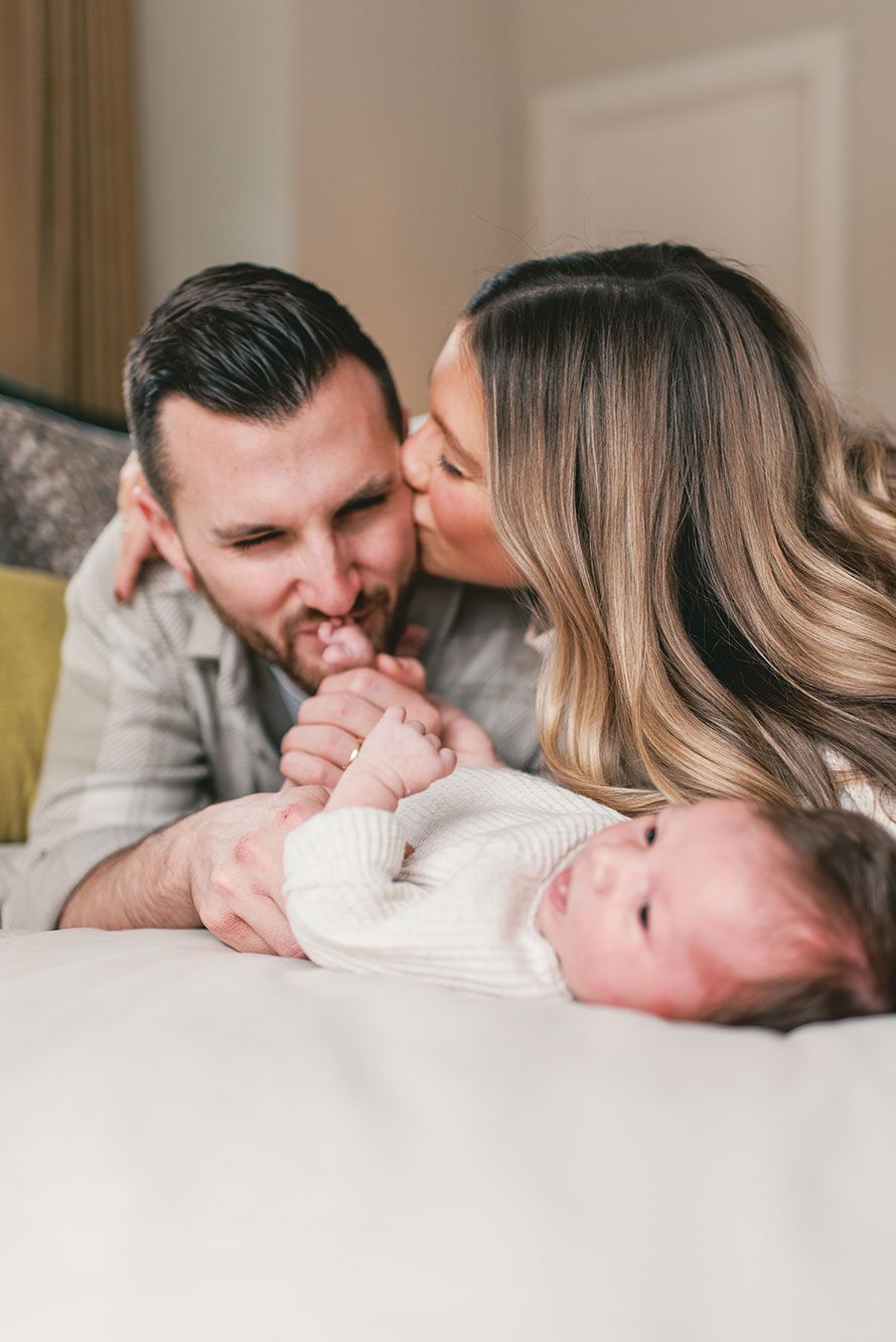 A series of intimate lifestyle photos showing parents lovingly bonding with their newborn baby on a white bed.