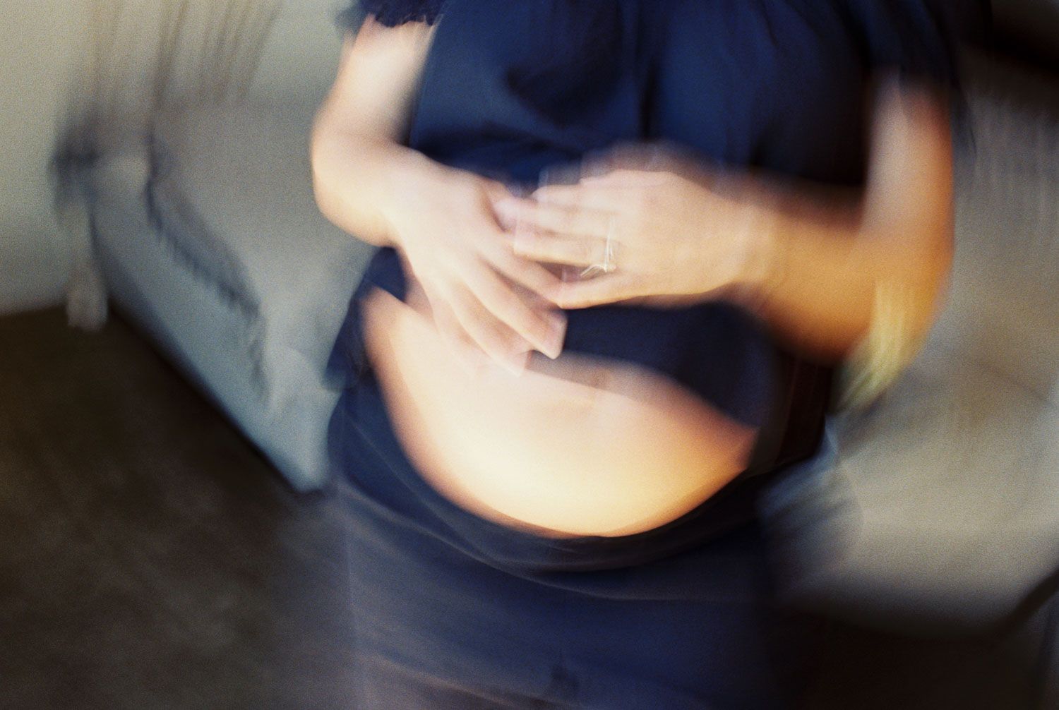Blurred motion photo of pregnant woman in blue dress cradling her baby bump with both hands.