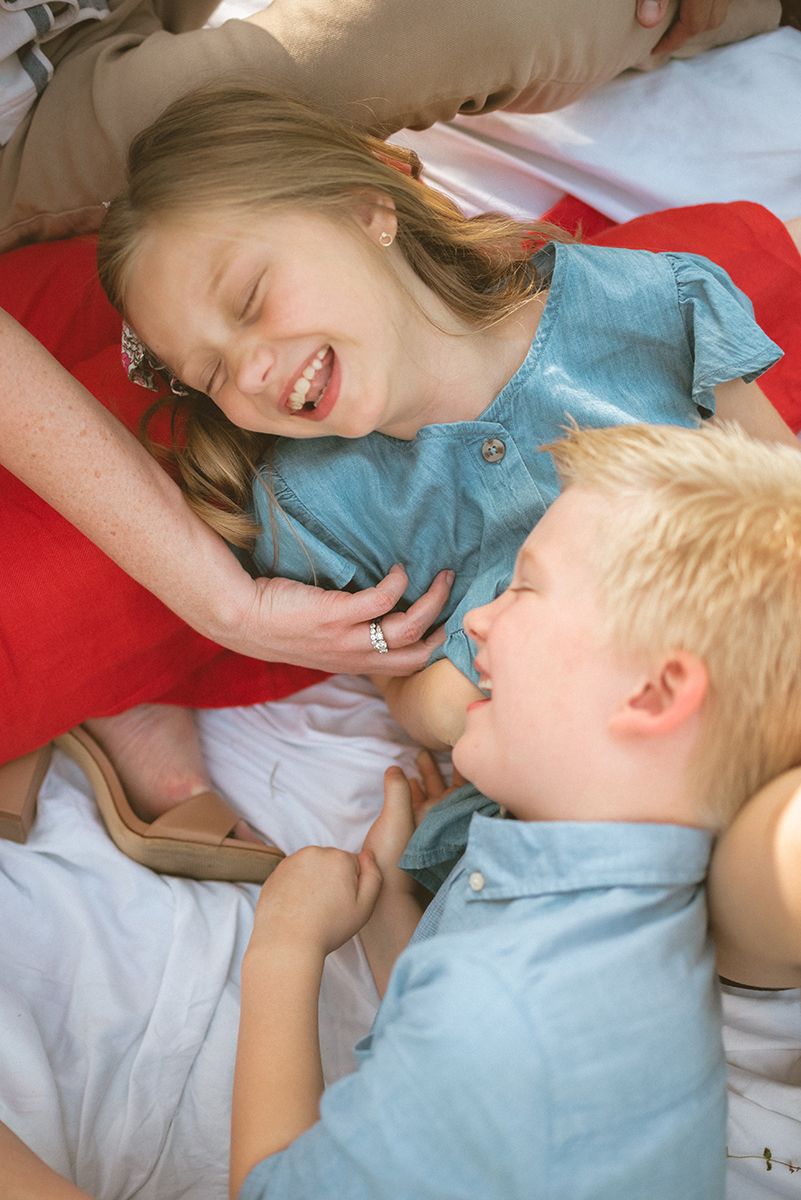 Two young children lie on a red blanket, laughing and smiling together as they share a playful and joyful moment.