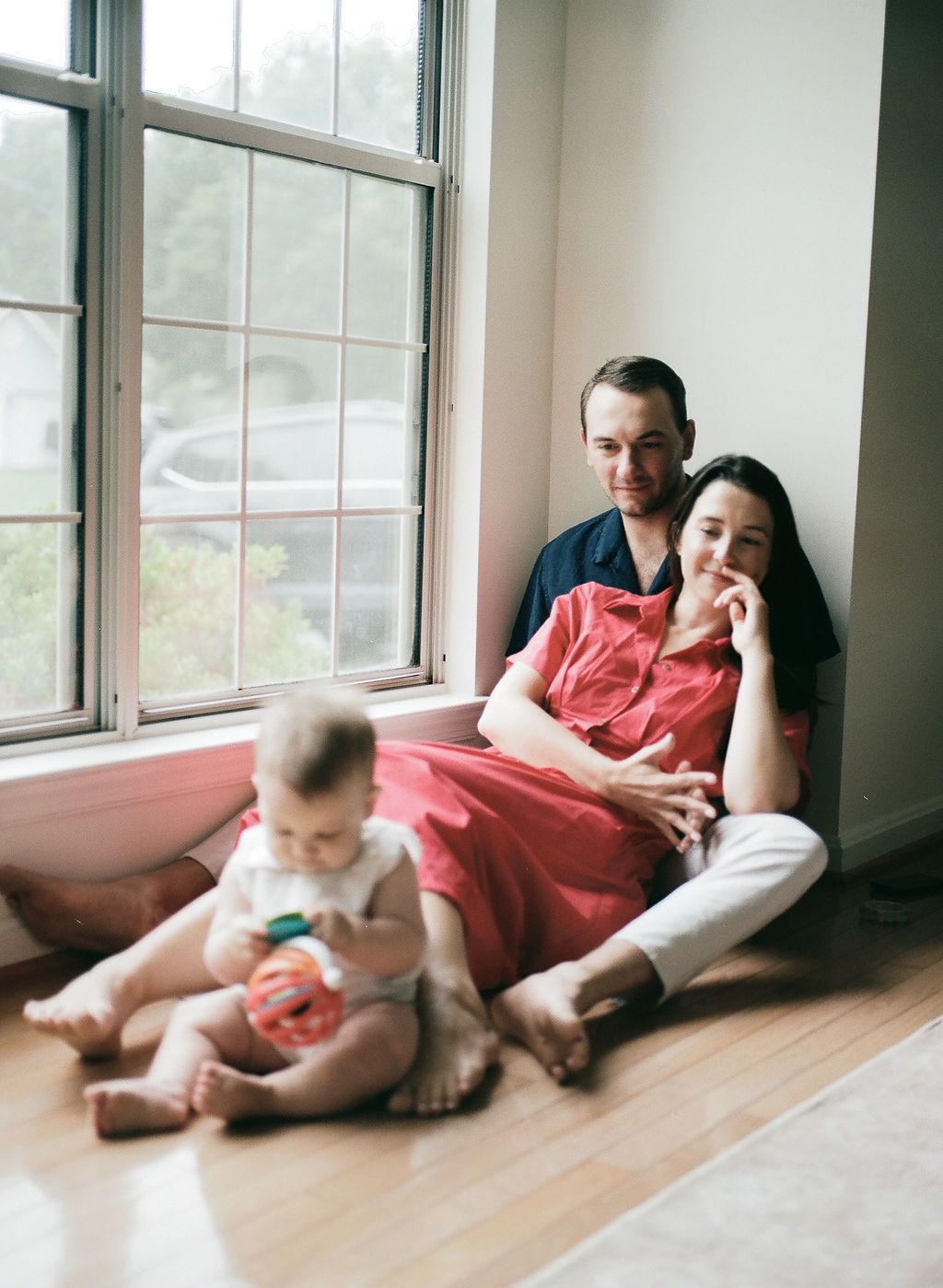 A sequence of photos showing a person and baby in coral-colored clothing resting on hardwood floors near windows.