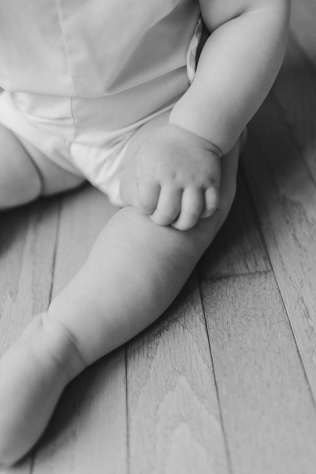 Baby's bare legs and feet resting on white wooden floor in soft black and white.