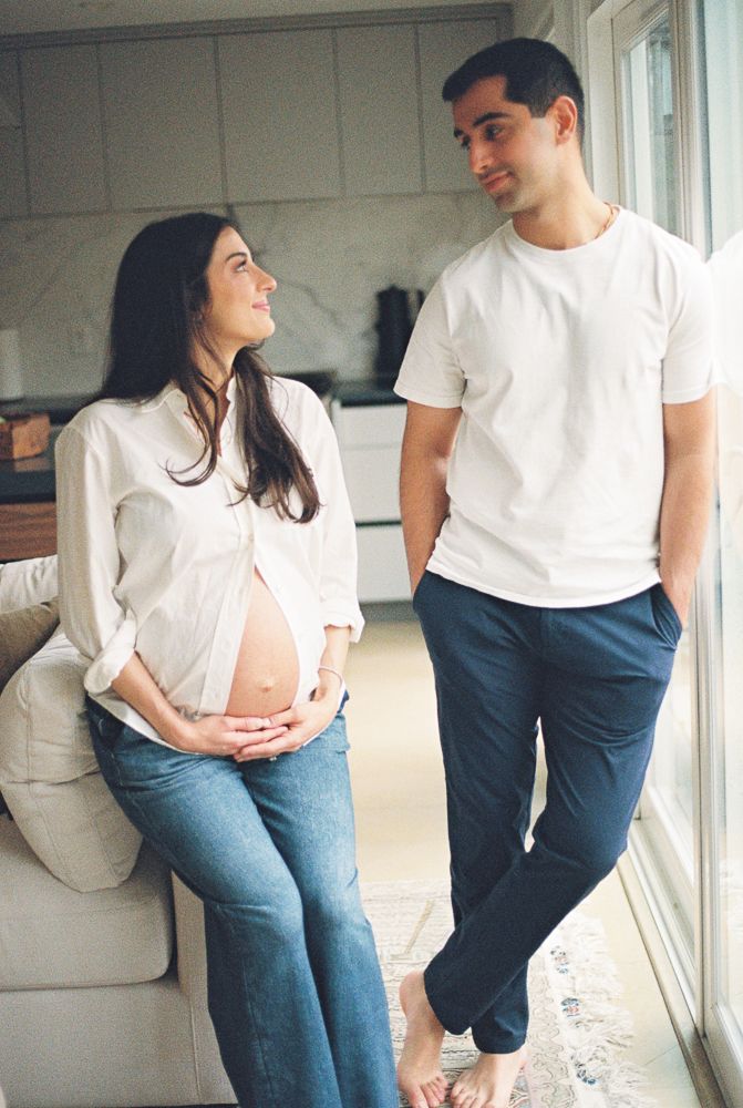 A couple in matching white shirts and blue jeans share intimate moments by a bright window in a photo series.