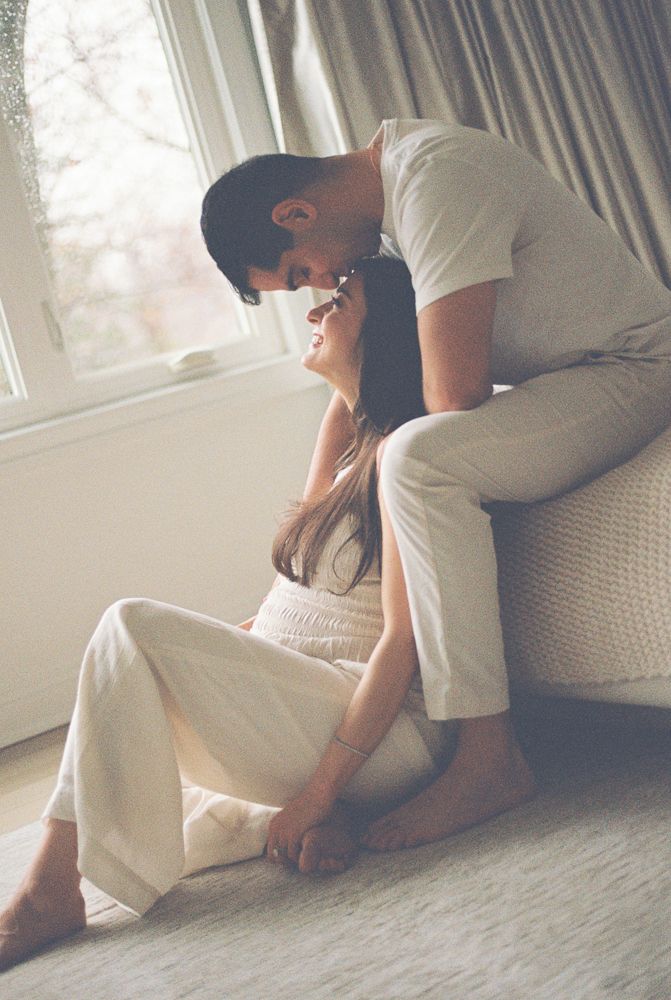 A romantic couple in white clothing sharing an intimate moment by a sunlit window.