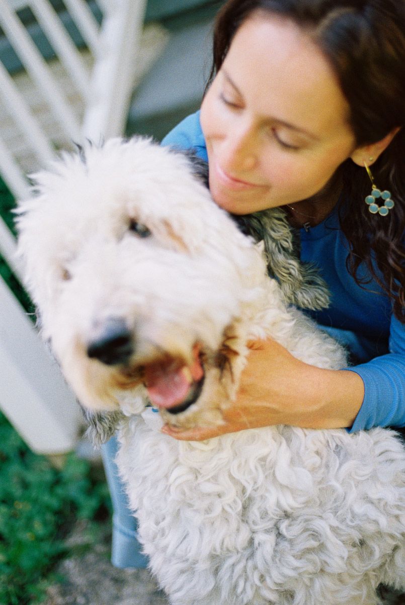 Woman in blue top hugging a fluffy white Goldendoodle dog outdoors.