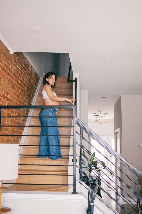 Person in blue jeans sits on wooden stairs with exposed brick wall and modern railing in contemporary interior space.
