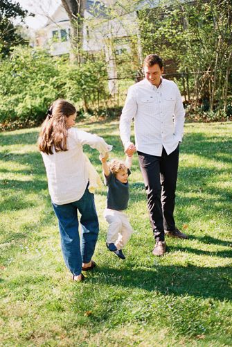 A smiling family with a young child plays together on a lush green lawn outdoors.