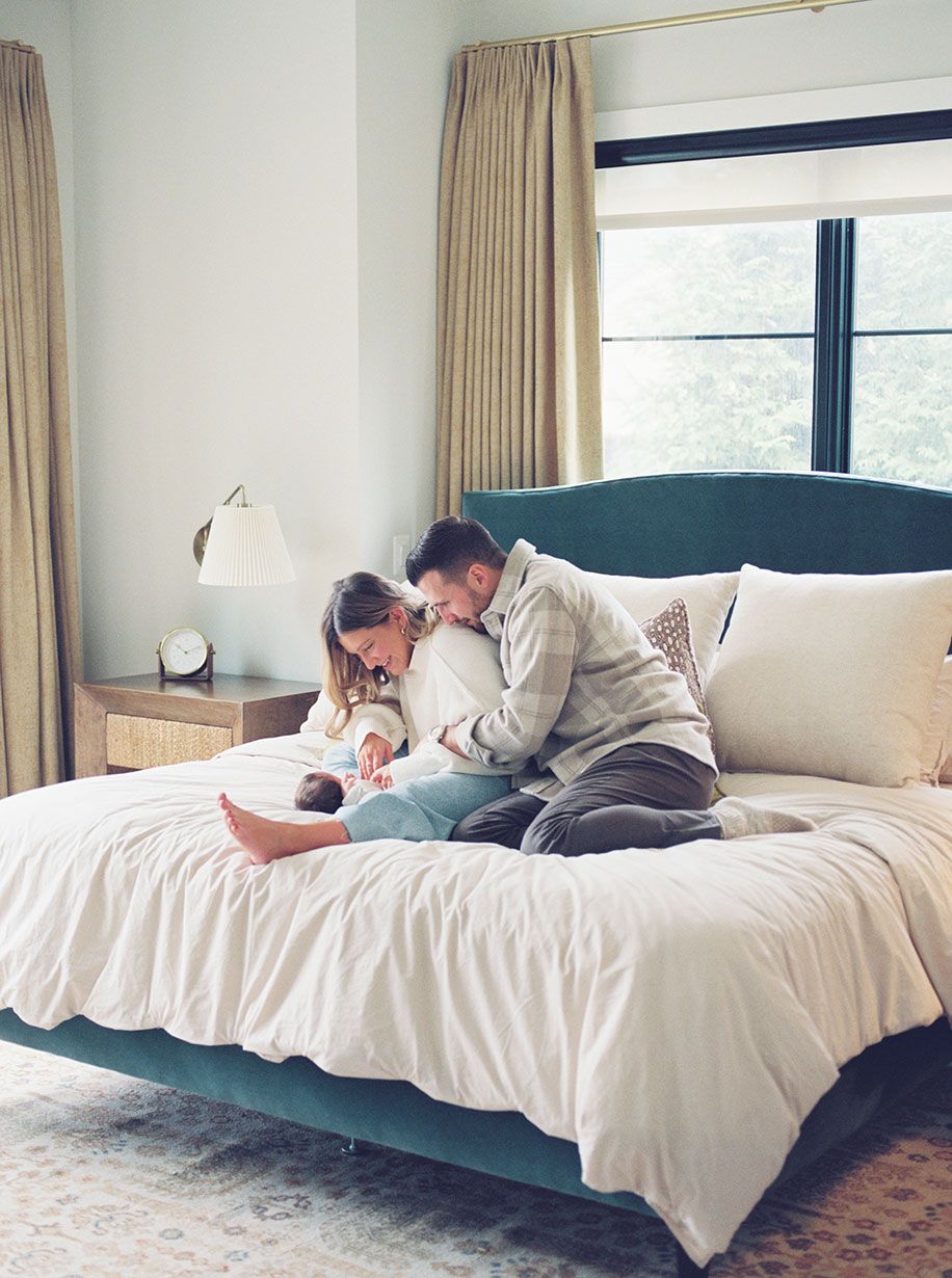 Family sharing tender moment together on bed with newborn baby in cozy bedroom with natural light.