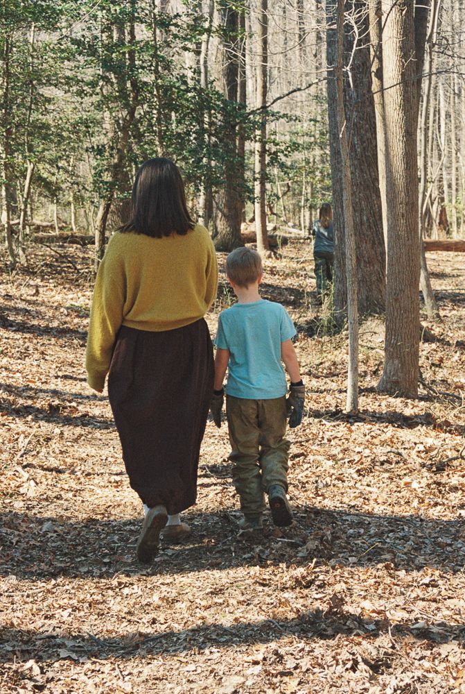 People walking together on a leaf-covered trail through a peaceful autumn forest on a sunny day.