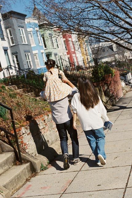 Two children walk up a sunny urban sidewalk past colorful row houses on a bright autumn day.