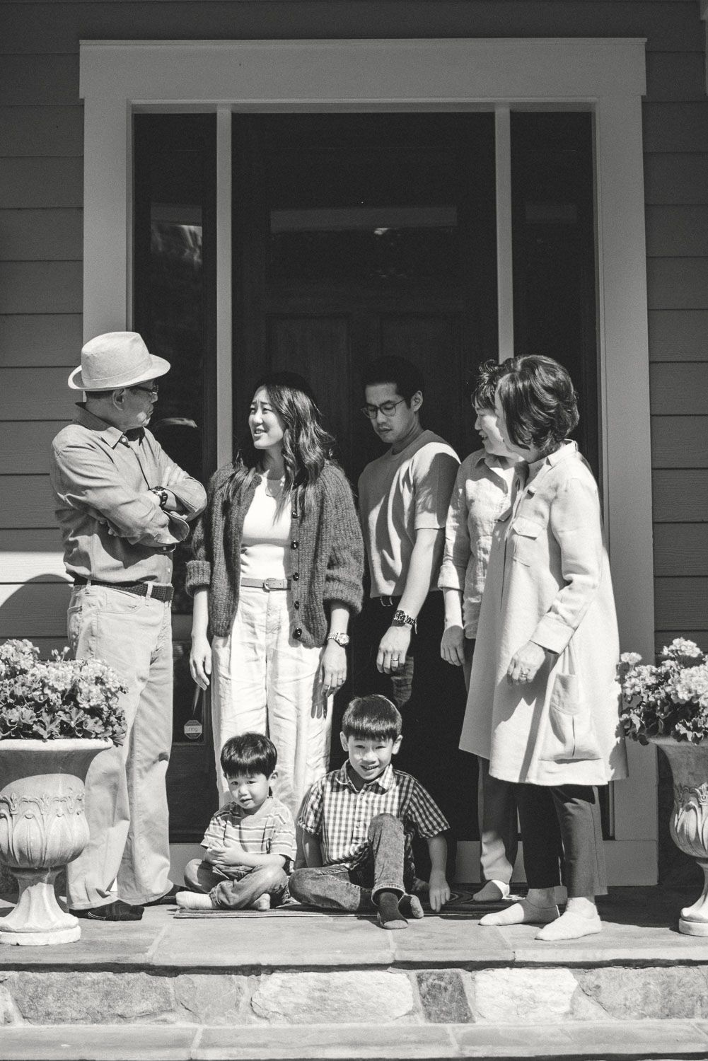 Black and white photo of a multigenerational Asian family posing on a home porch, including two young children seated on steps.