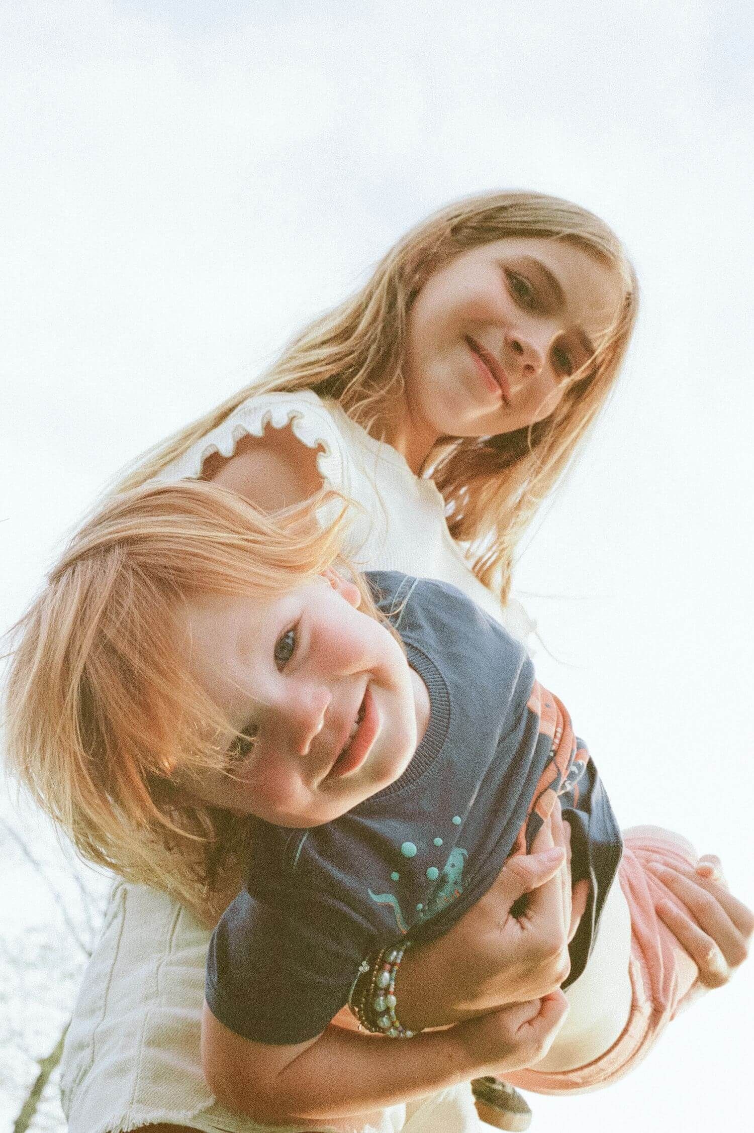 Two figures photographed from below against bright sky in casual attire share a light-hearted moment together.