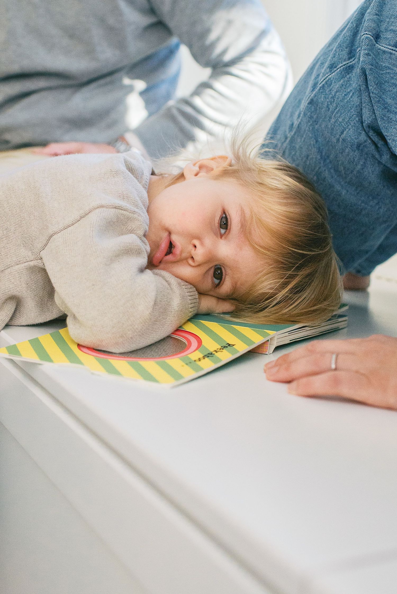 A child rests their head on a colorful striped pillow while lying on a white surface.