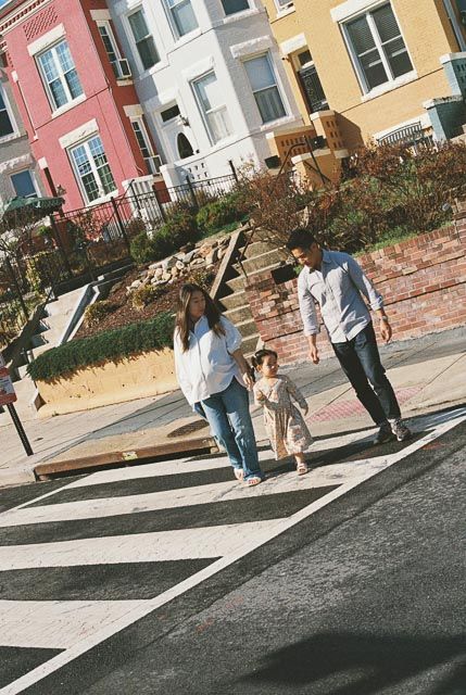 Family with toddler crossing a zebra crossing on a colorful urban street on a sunny day.