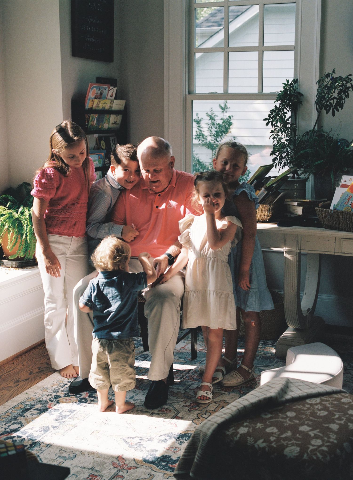 A series of five photos showing a child and adult sitting together on the floor in sunlit room looking at something below.
