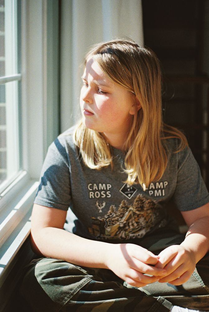 A person in a dark gray Camp t-shirt sits by a window in a contemplative sequence of four similar poses.