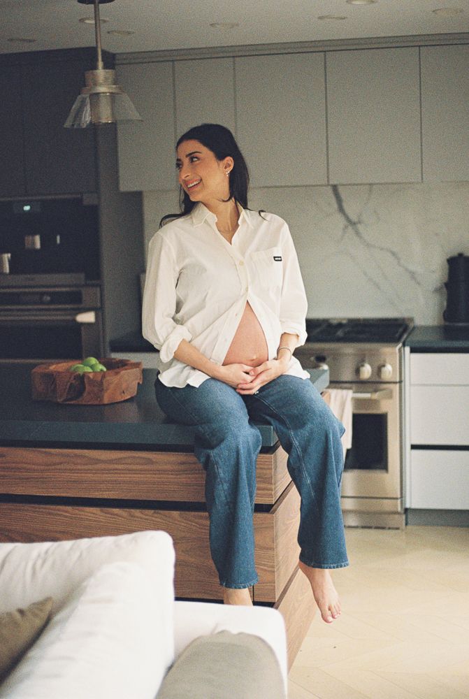 Person in white shirt and blue jeans sits casually on wooden bench in modern kitchen with marble accents.