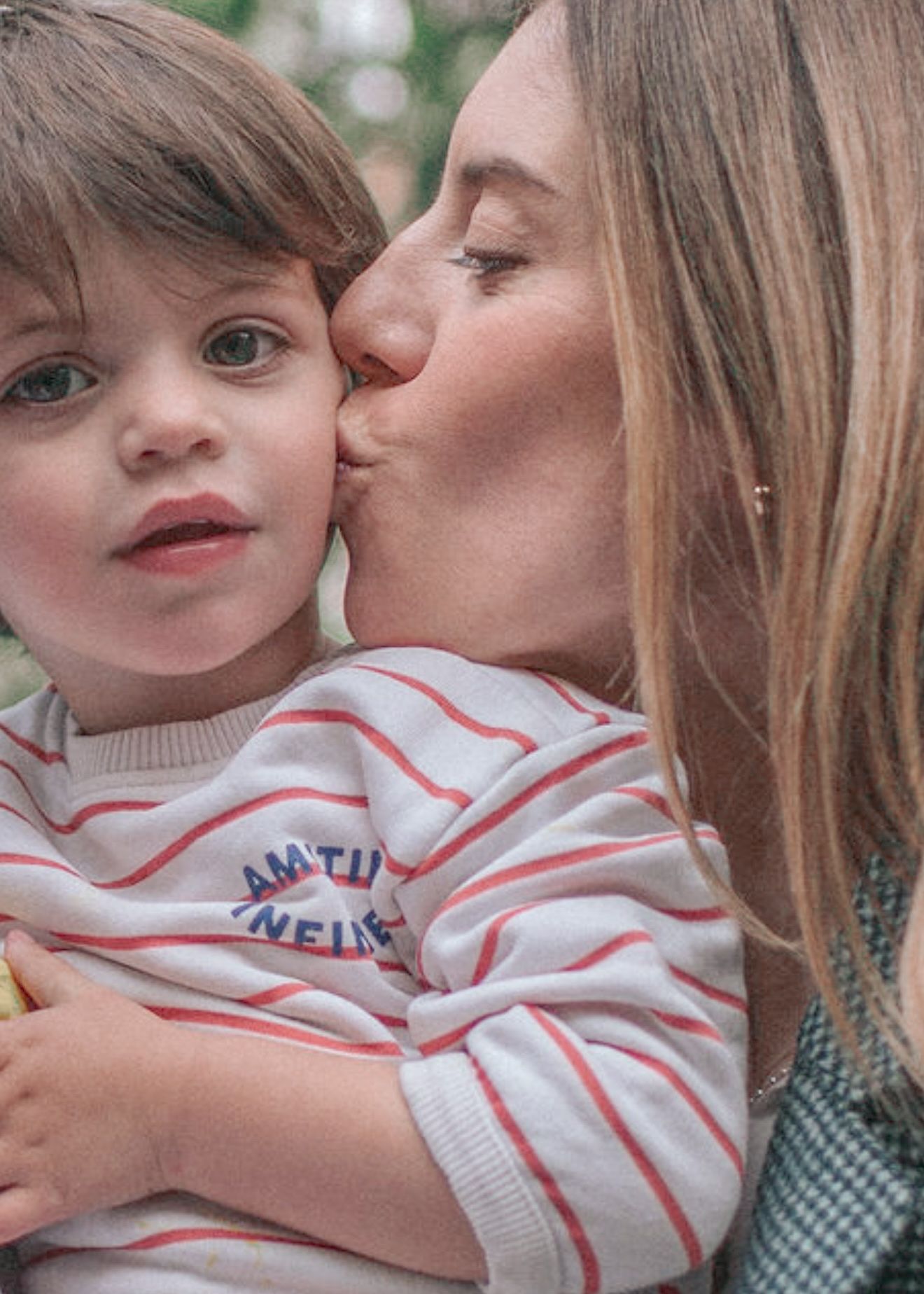 A tender moment captured between parent and child wearing a striped sweater against a soft green background.