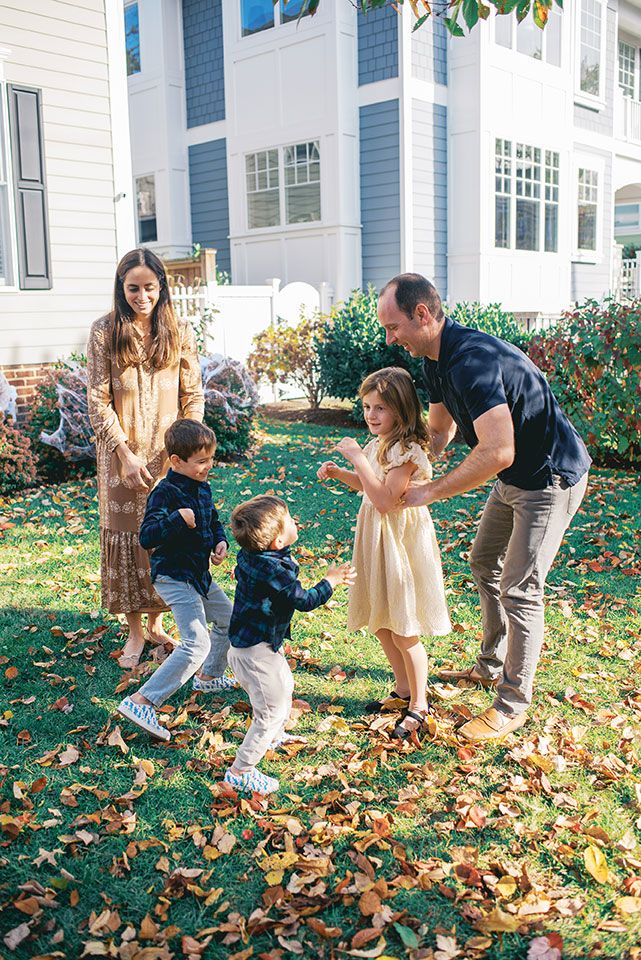 People playing together in fallen autumn leaves on a sunny day outside a white house.