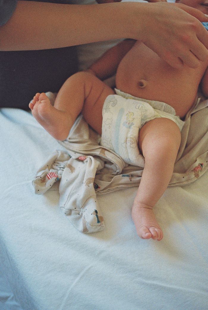 A baby in a diaper lying on a white surface during a diaper change with an adult's hands visible.