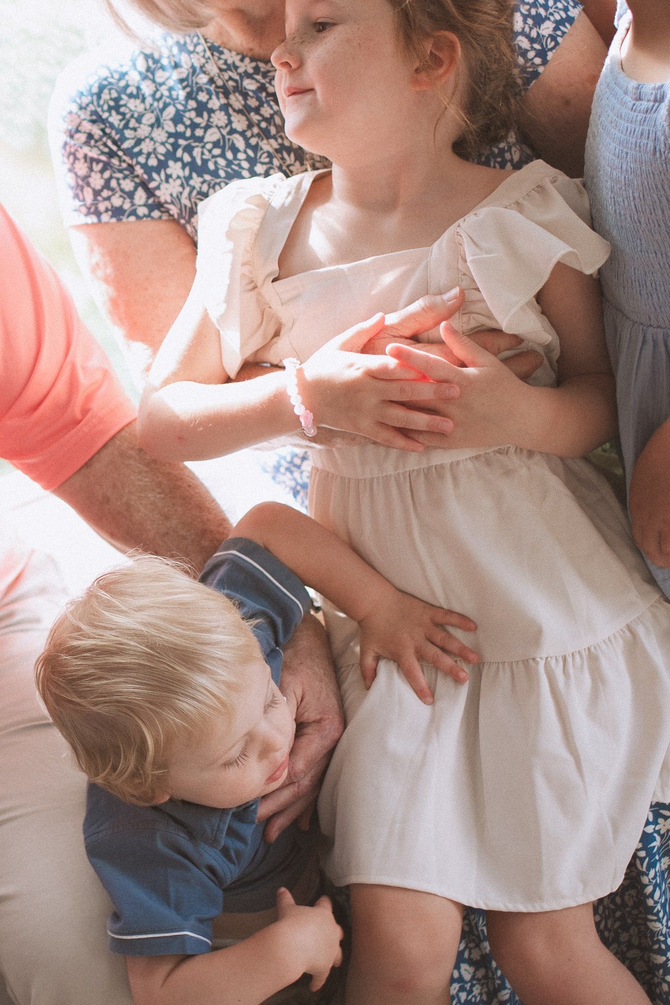 Siblings in casual clothing share a sweet family moment together on a couch in soft lighting.