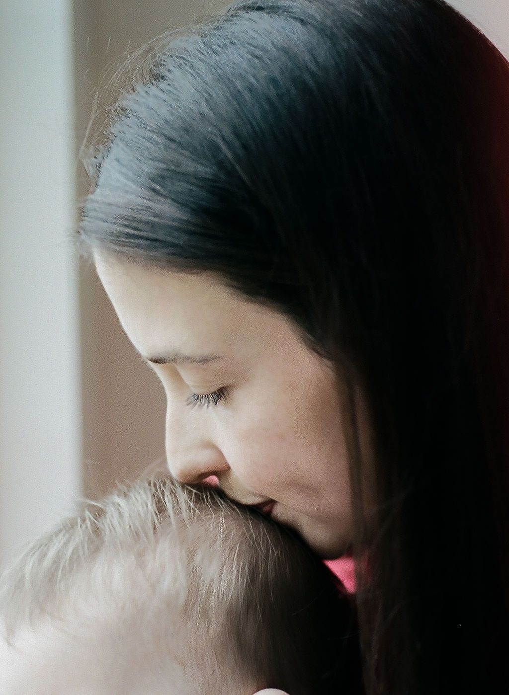 Silhouetted profile of a parent showing affection to their baby in a soft, intimate portrait.