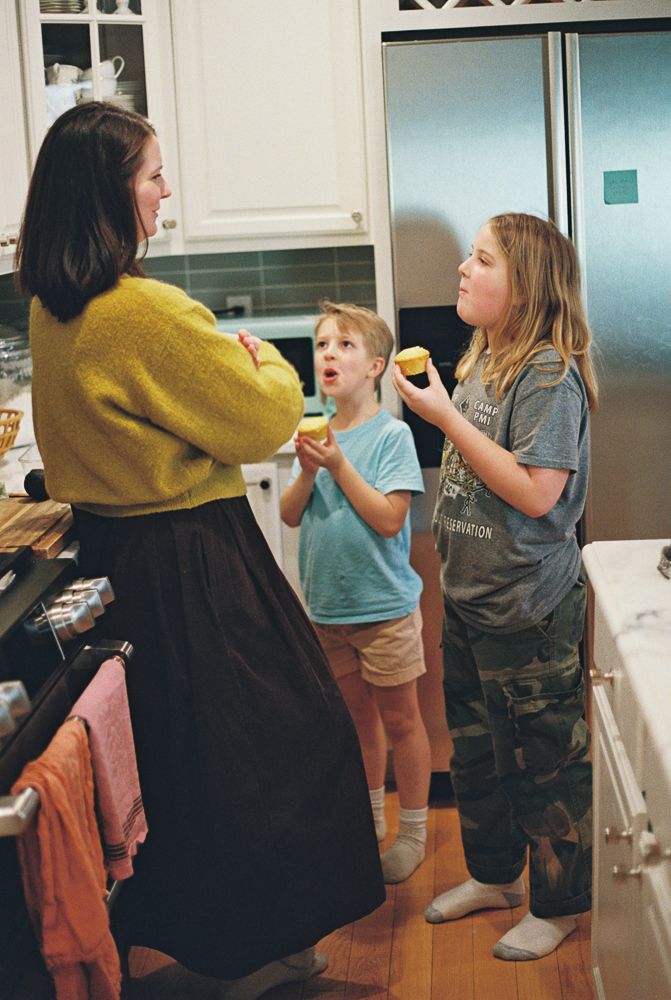 People gathered in a kitchen having an animated conversation while standing near appliances and cabinets.