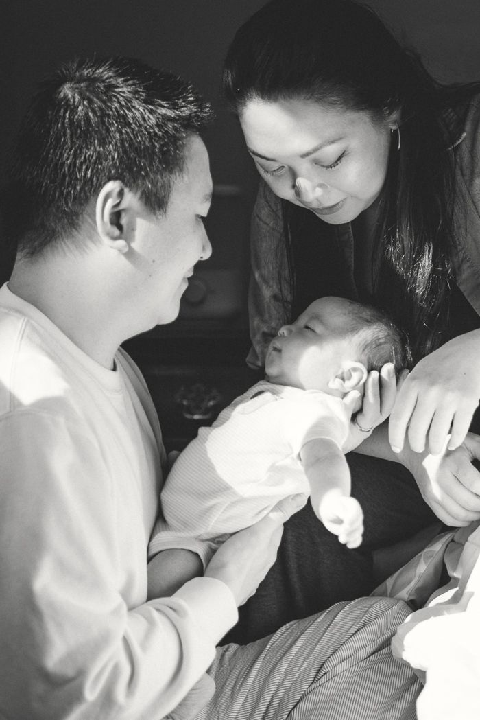 Black and white photo of two parents lovingly gazing at their newborn baby held in fathers arms.