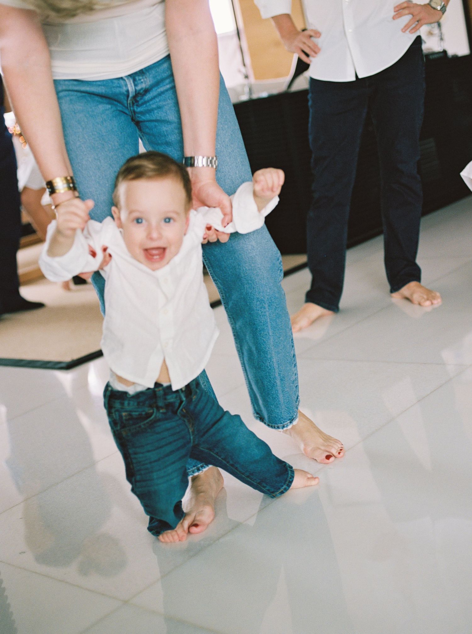 A sequence of photos showing a toddler learning to walk while holding hands with someone in jeans.