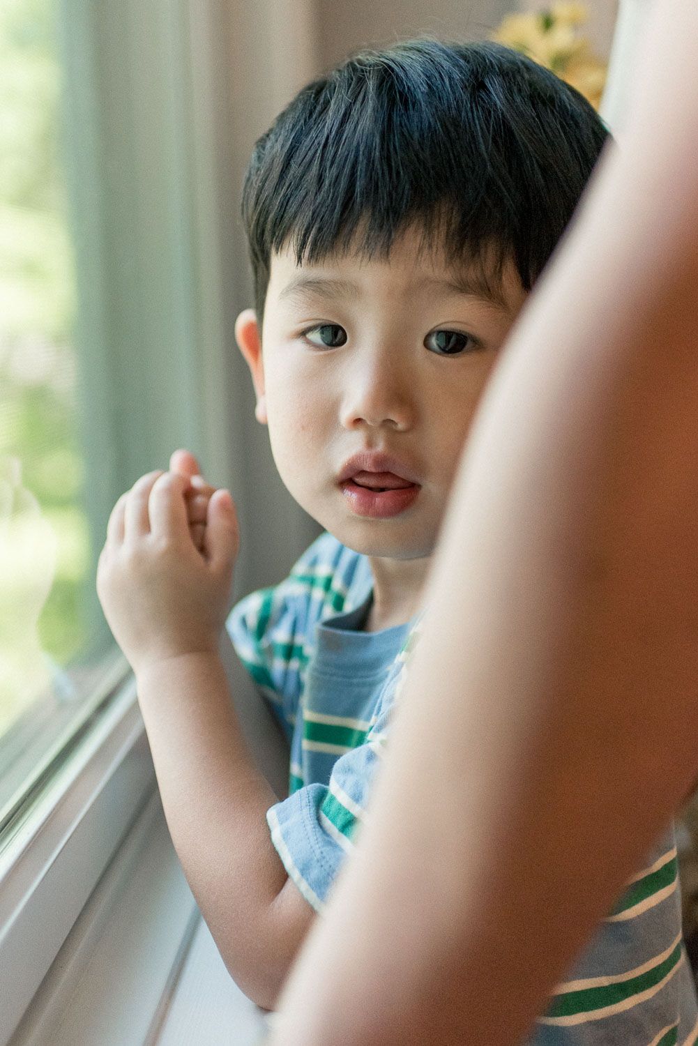 Close-up of a young Asian boy looking out a window with a curious expression on his face.