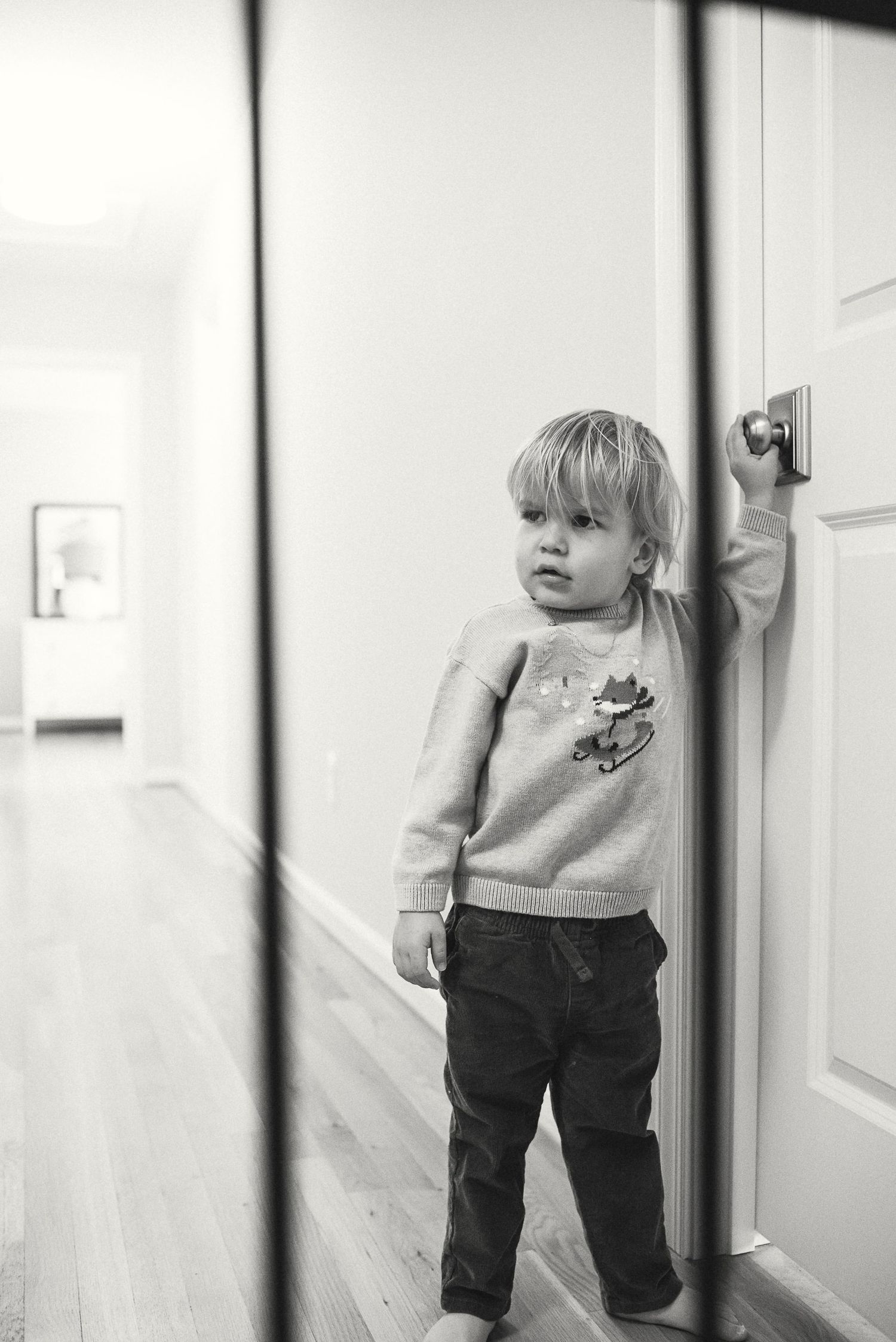 Toddler in gray sweater and dark pants peeks around white door frame in three sequential photos.