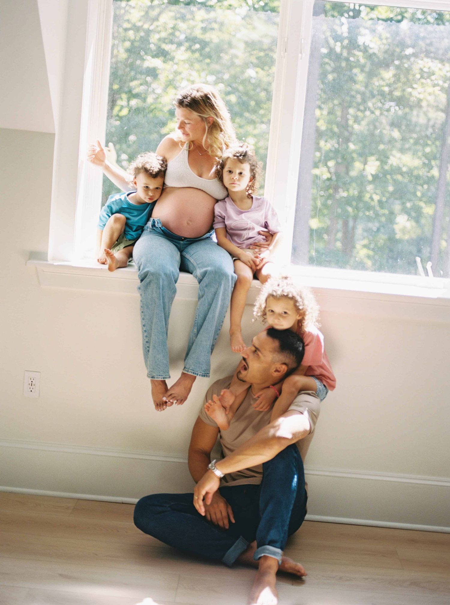 Family sitting together by a bright window in an empty room.