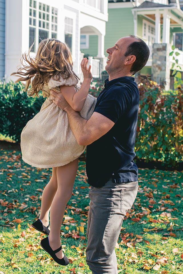 A playful moment captured outdoors as a parent lifts and spins a child wearing a beige dress in a garden setting.