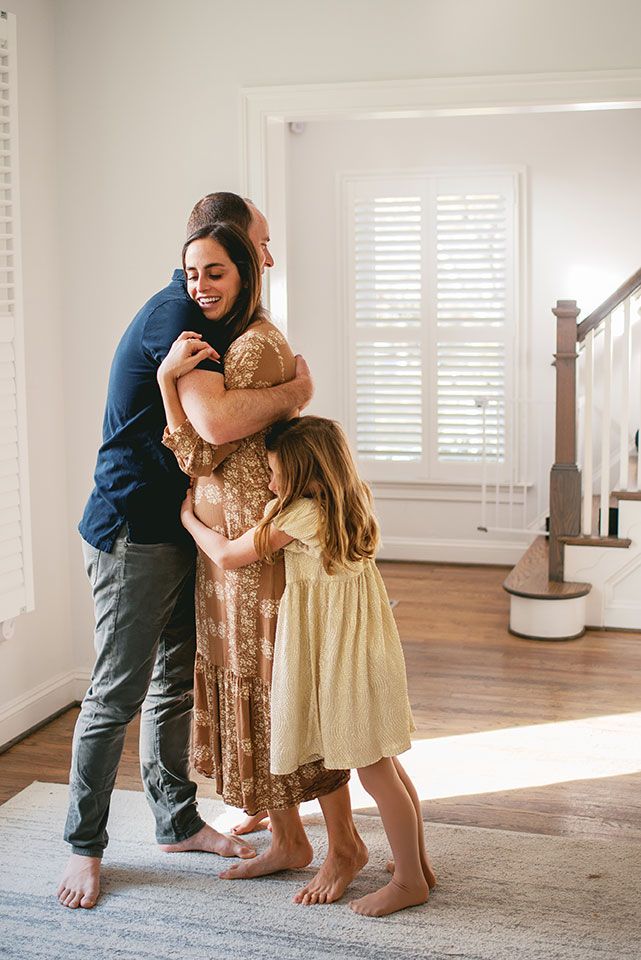 A tender family moment captured in a bright white room with hardwood floors and a gray rug.