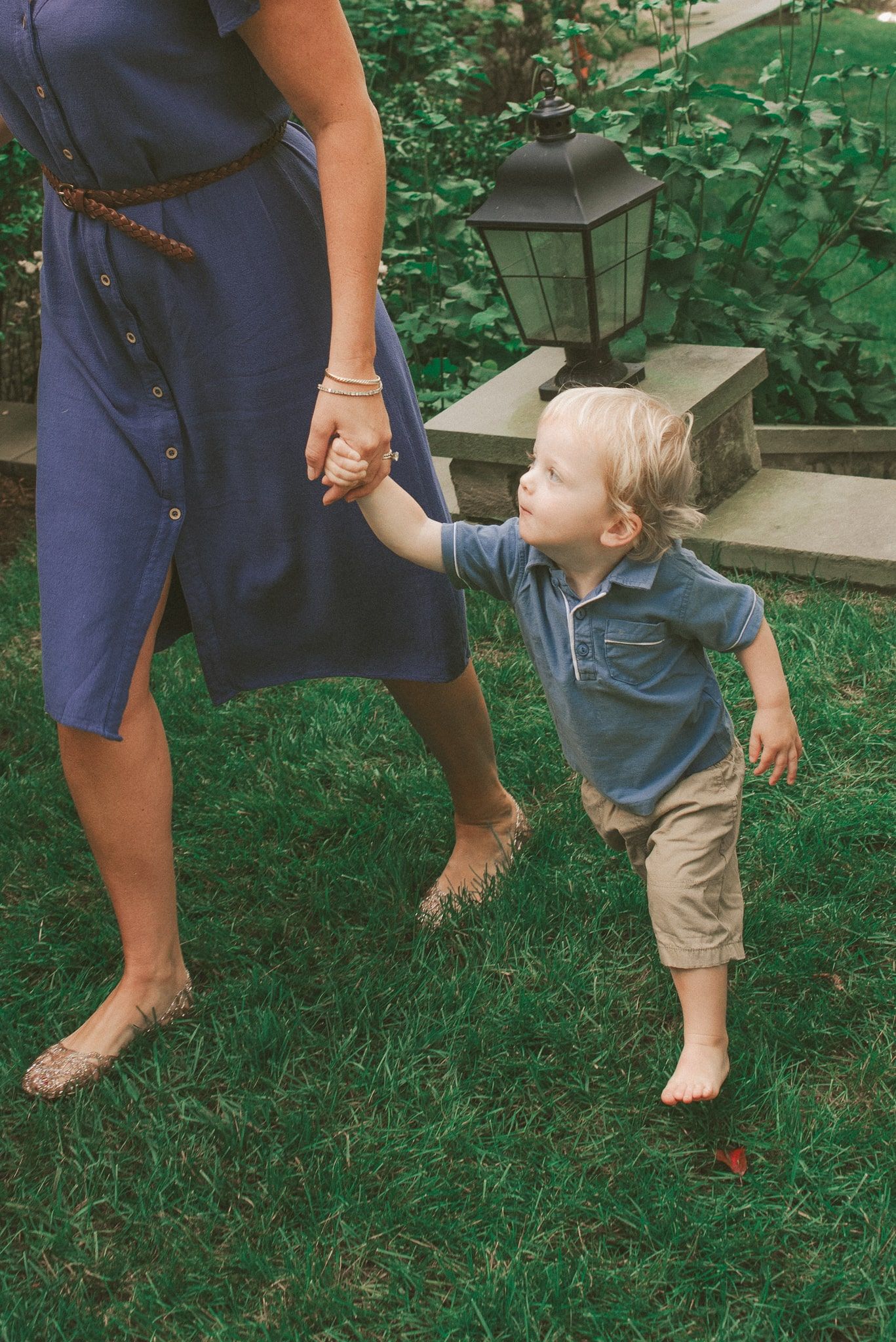 A series of photos showing a toddler in khaki shorts playing and walking in grass next to someone in a navy dress.