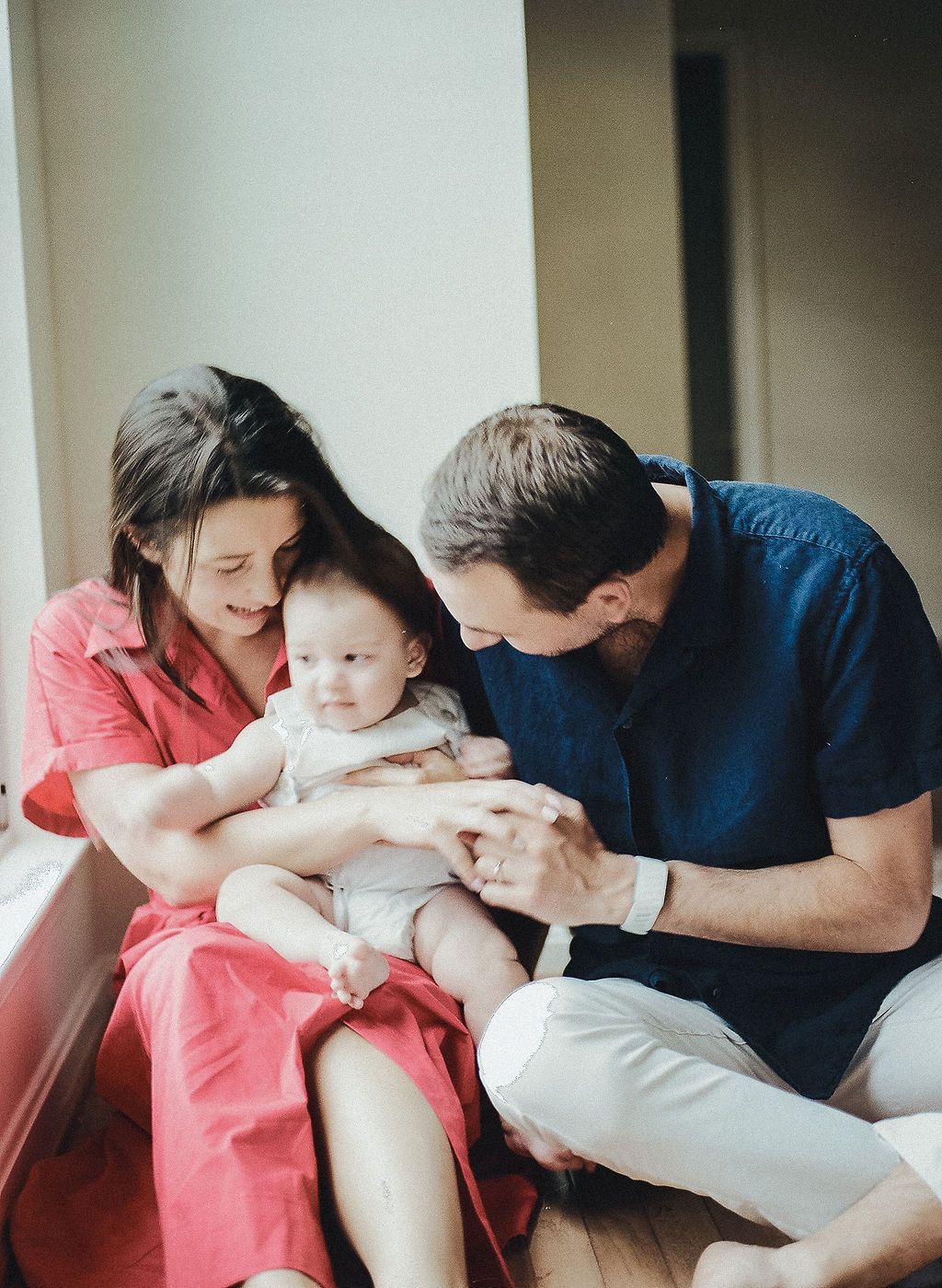 A series of photos showing a tender moment as parents cuddle and kiss their baby in a bright room.