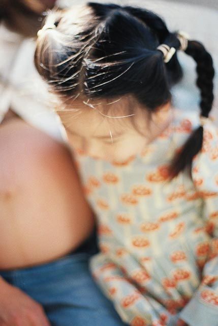 Young girl with dark pigtails wearing a floral print top, photographed from above in soft focus.
