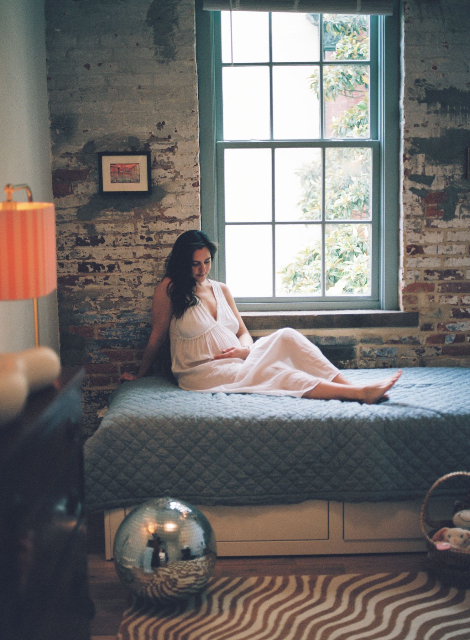 A cozy reading nook with vintage brick walls and large windows features a window seat and lamp creating a warm atmosphere.