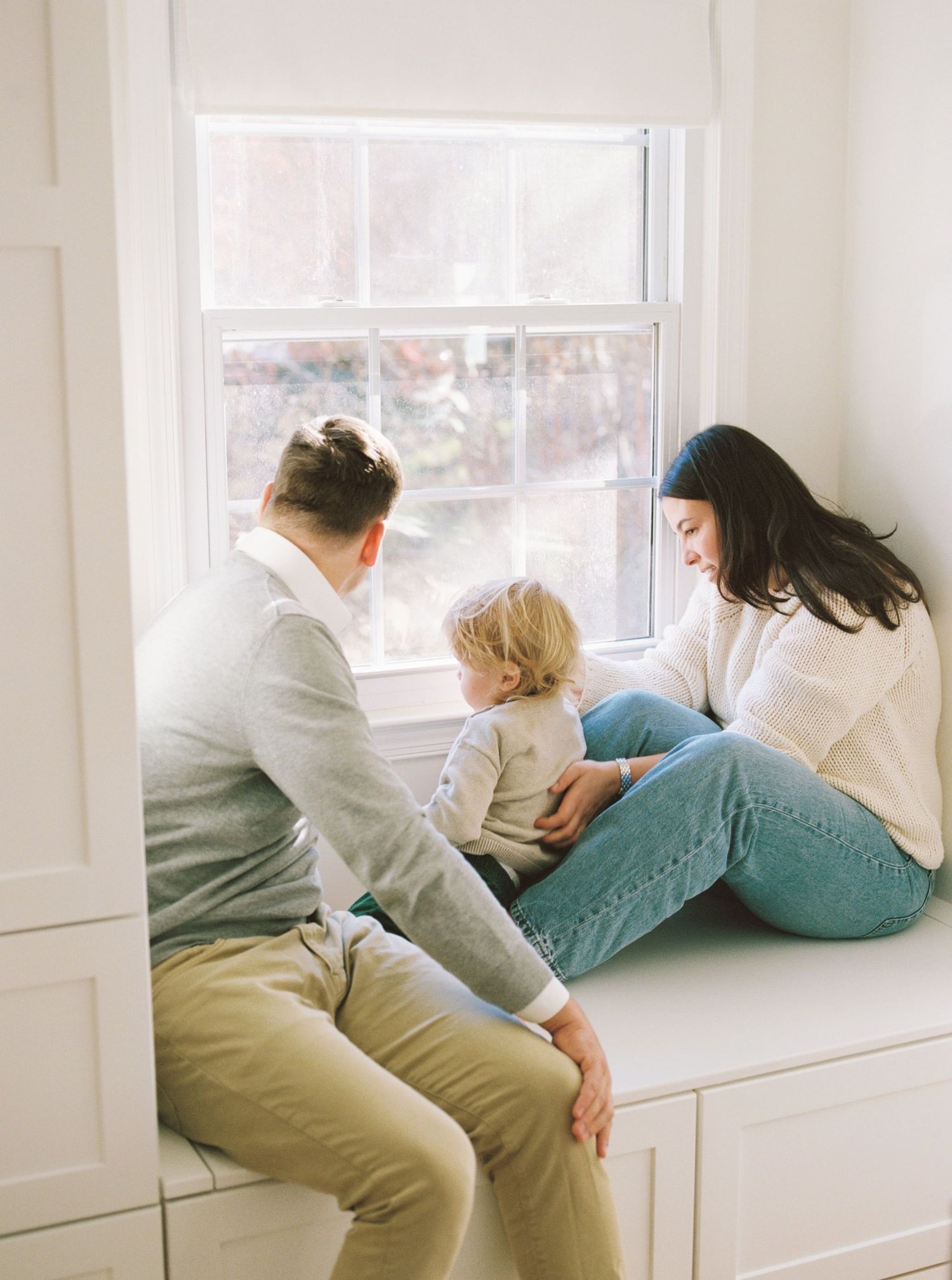 A family sits together on a window seat, looking out at the view on a bright day.